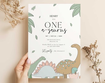 May include: A white dinosaur-themed birthday party invitation with green leaves and colorful dinosaurs. The text reads "Henry is a One-a-saurus" with the date and time of the party, RSVP information, and the phrase "Let's party like dinosaurs!"