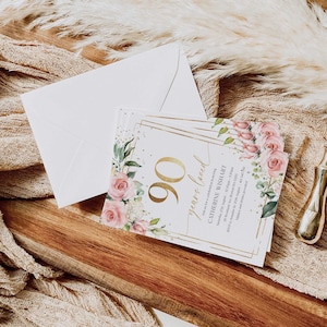 May include: A white invitation card with gold accents and floral designs. The text on the card reads "90 years loved" and "Catherine Wishart".