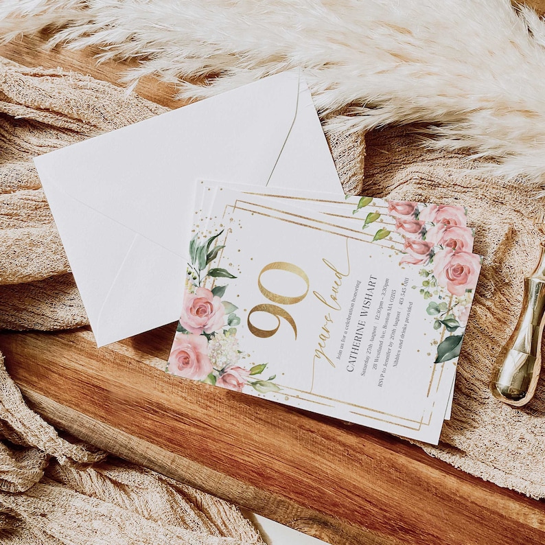 May include: A white invitation card with gold accents and floral designs. The text on the card reads "90 years loved" and "Catherine Wishart".