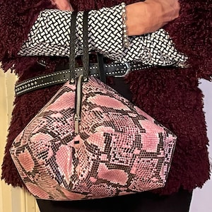 May include: A pink and black snakeskin handbag with a zipper closure. The bag has a triangular shape and is made of a textured material.