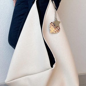 May include: A large, off-white tote bag with a black lining. The bag has a silver chain with a star-shaped charm attached to it.