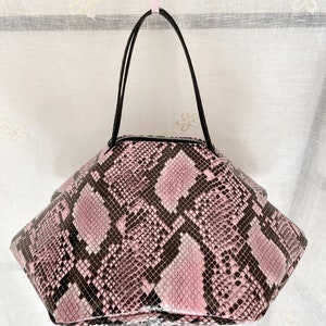 Könnte beinhalten: Eine rosa und schwarze Schlangenleder-Handtasche mit einem schwarzen Henkel.