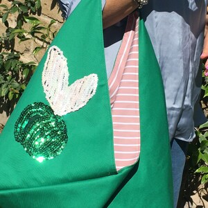 May include: A green tote bag with a pink and white striped lining. The bag has a large green sequin applique of a fruit with a white sequin applique of a leaf.