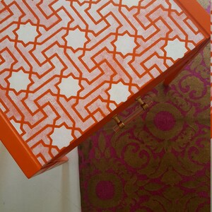 May include: Orange side table with a white geometric pattern stencil design. The table has a single drawer with a gold handle.