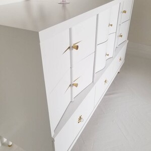 May include: White dresser with six drawers and gold-toned hardware. The dresser has a modern design with curved edges and a sleek finish.