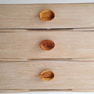 May include: A white dresser with four drawers and wooden knobs. The dresser has a light wood grain finish.