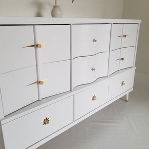 May include: White dresser with six drawers and gold-toned hardware. The dresser has a curved front and sits on tapered legs.