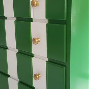 May include: A white and green chest of drawers with four drawers and gold knobs. The dresser has a chequered pattern.
