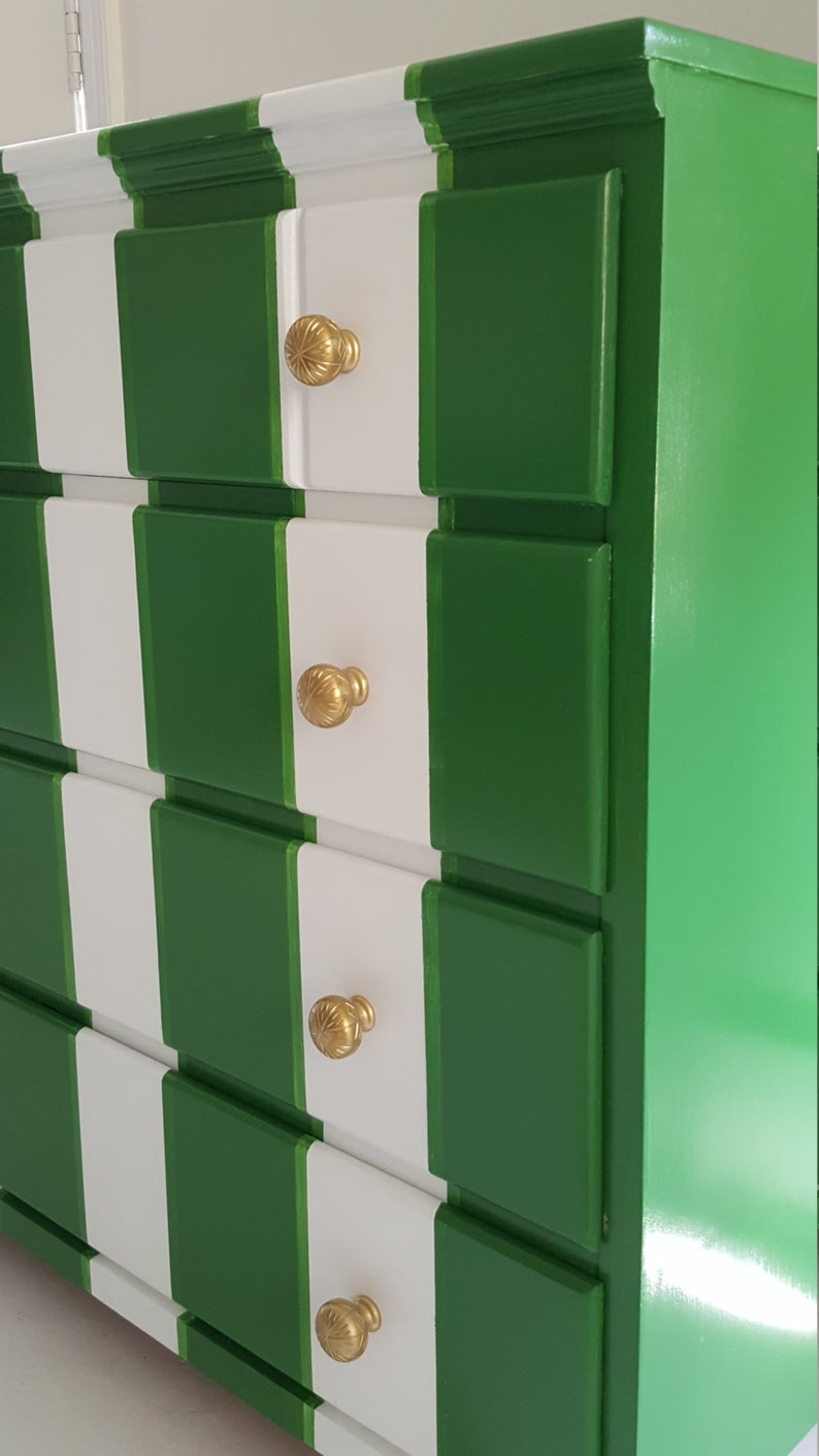 May include: A white and green chest of drawers with four drawers and gold knobs. The dresser has a chequered pattern.