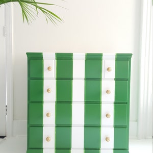 May include: A green and white striped chest of drawers with four drawers and gold knobs. The dresser has a traditional style and is made of wood.