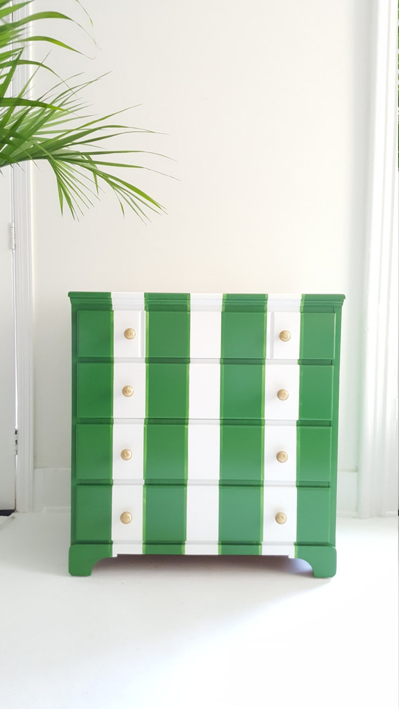 May include: A green and white striped chest of drawers with four drawers and gold knobs. The dresser has a traditional style and is made of wood.