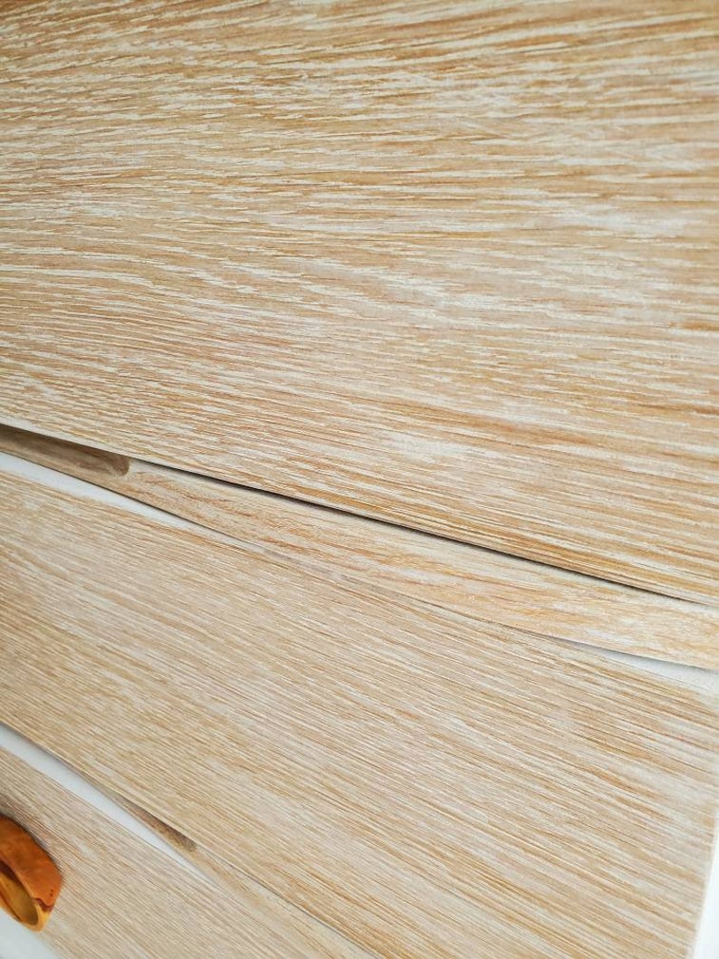 May include: Close-up of a light wood dresser with three drawers. The drawers have a whitewashed finish and a slightly curved edge.