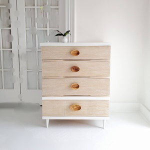 May include: A white dresser with five drawers and wooden knobs. The dresser has a light wood grain finish and sits on white legs.