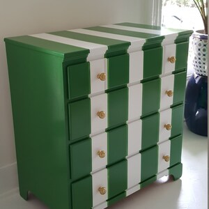 May include: A green and white striped chest of drawers with four drawers and gold knobs. The chest of drawers has a traditional style and is painted in a bold colour scheme.
