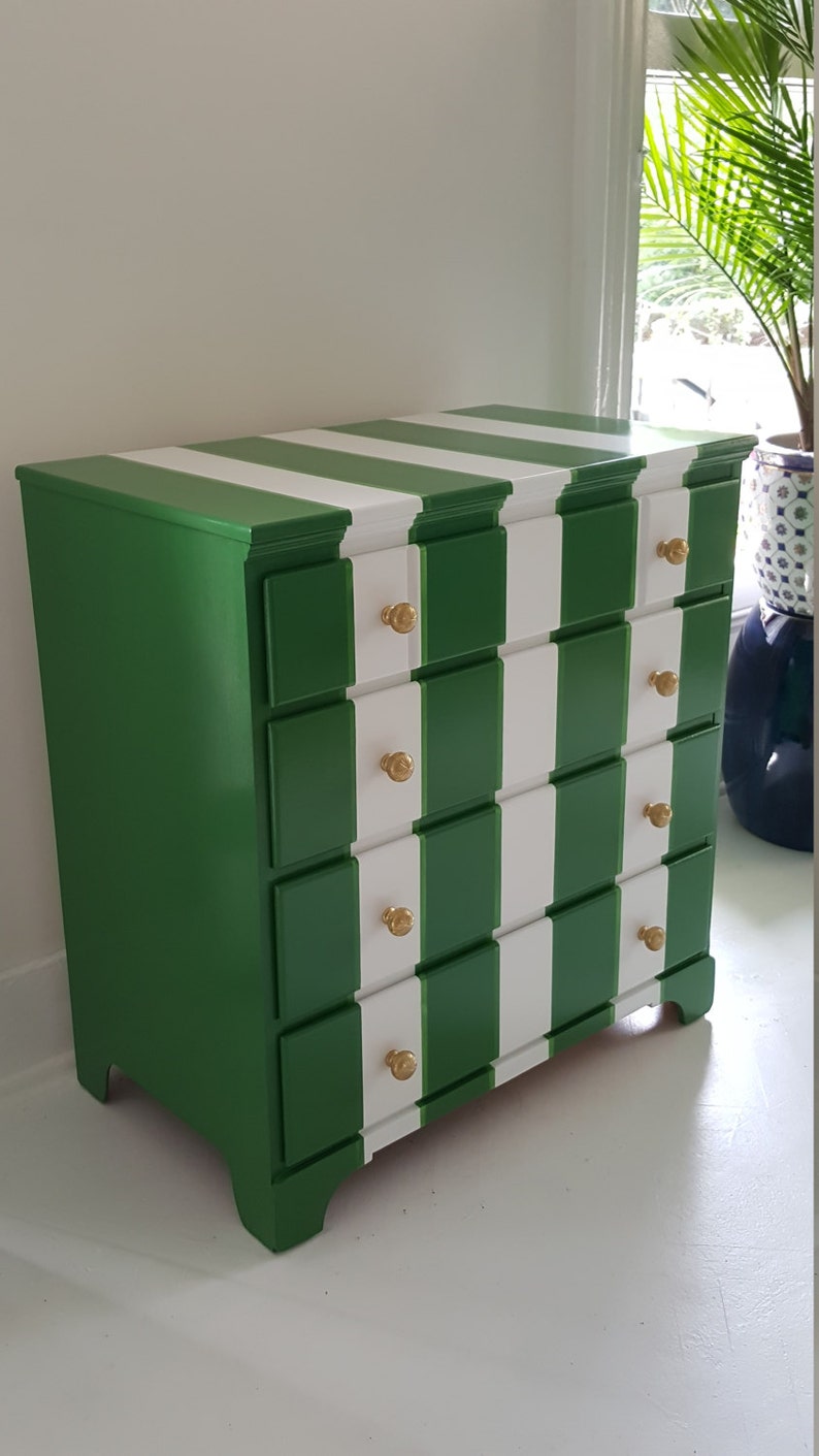 May include: A green and white striped chest of drawers with four drawers and gold knobs. The chest of drawers has a traditional style and is painted in a bold colour scheme.