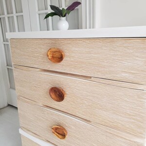 May include: A white dresser with four drawers and wooden knobs. The dresser has a light wood grain finish.