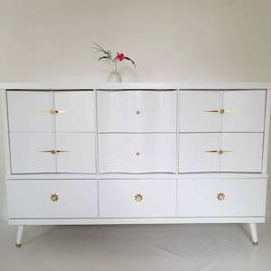May include: White dresser with six drawers and gold hardware. The top three drawers have a wavy design. The bottom three drawers have star-shaped knobs.