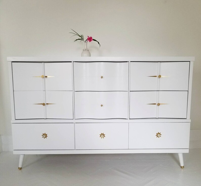 May include: White dresser with six drawers and gold hardware. The top three drawers have a wavy design. The bottom three drawers have star-shaped knobs.