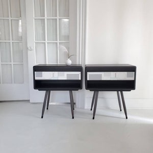 May include: Two black nightstands with white geometric designs and four black legs. The nightstands are on a white floor.