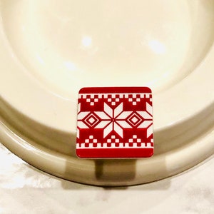 May include: White ceramic bowl with a raised rim and a small hole in the center. A red and white patterned square sticker is attached to the bottom of the bowl.