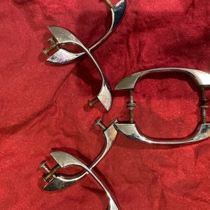 May include: Three silver-toned cabinet door handles with a decorative design. The handles are on a red fabric background.