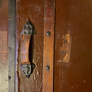 May include: A vintage wooden suitcase with a leather handle and metal hardware. The suitcase has a label that says "Cunard" and another label with the numbers "86" and "8863".