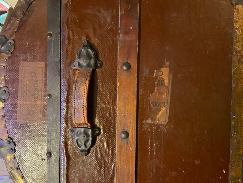 May include: A vintage wooden suitcase with a leather handle and metal hardware. The suitcase has a label that says "Cunard" and another label with the numbers "86" and "8863".