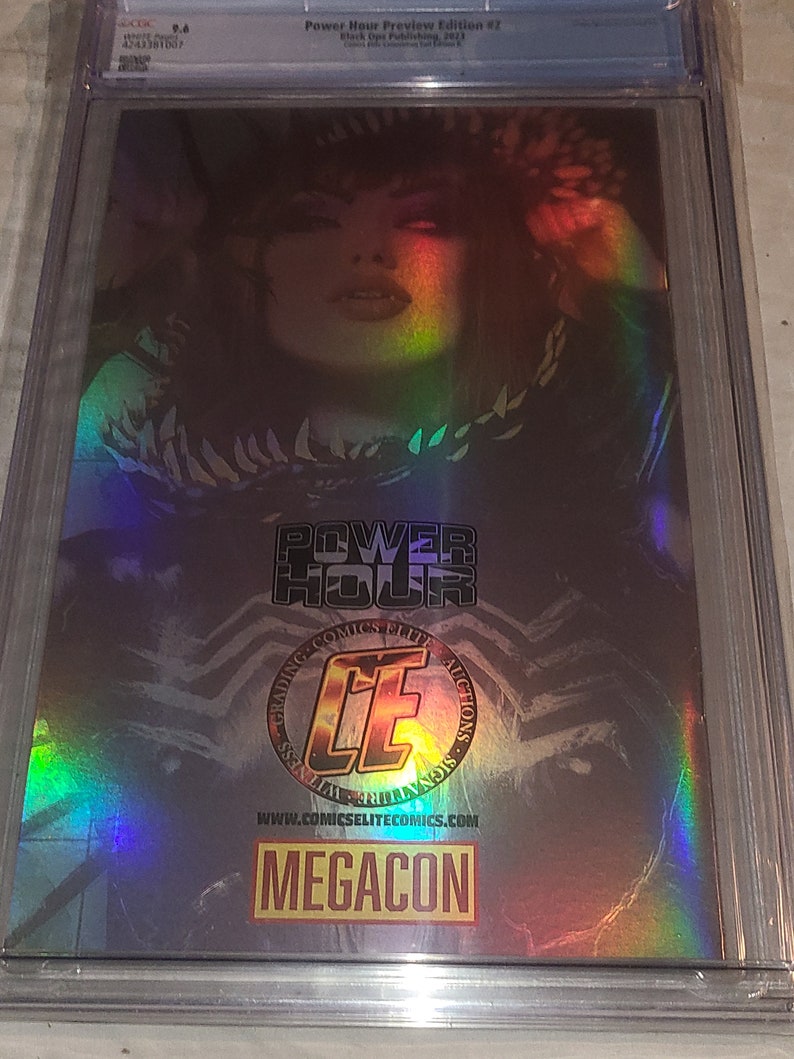 May include: A holographic comic book cover featuring a woman with dark hair and red eyes. The cover has a rainbow iridescent effect and the text "Power Hour Preview Edition #2" and "Black Ops Publishing 2023".