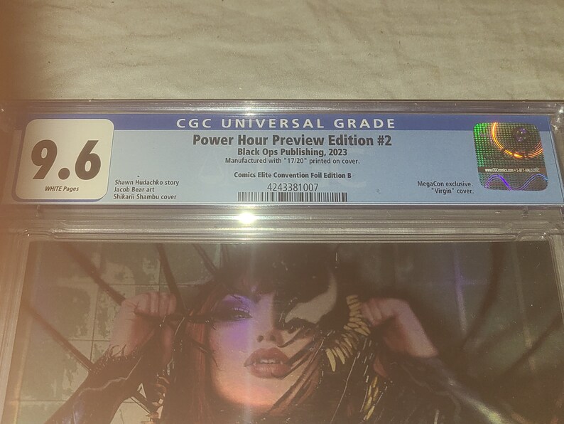 May include: A graded comic book with a 9.6 rating. The comic book is titled "Power Hour Preview Edition #2" and is published by Black Ops Publishing in 2023. The comic book is a MegaCon exclusive with a "Virgin" cover.