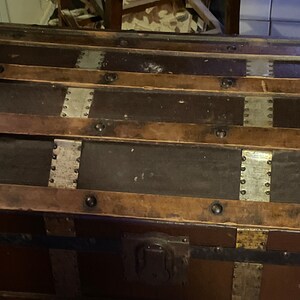 May include: A vintage wooden trunk with metal accents and leather straps. The trunk has a dark brown finish and is decorated with silver and brass hardware.