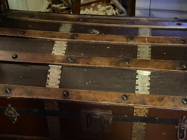 May include: A vintage wooden trunk with metal accents and leather straps. The trunk has a dark brown finish and is decorated with silver and brass hardware.