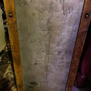 May include: A vintage wooden trunk with a metal lid. The lid has a worn, gray surface with scratches and marks. The trunk has brown wooden sides and metal accents.