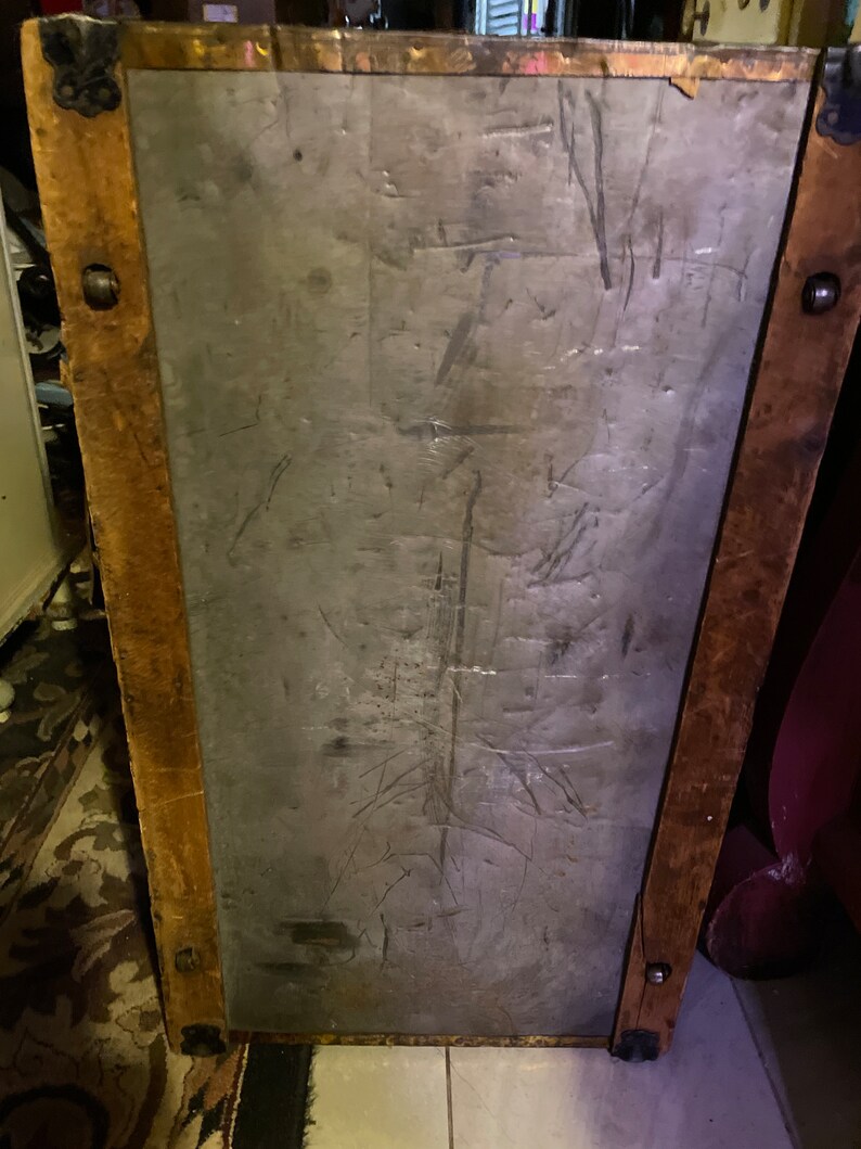 May include: A vintage wooden trunk with a metal lid. The lid has a worn, gray surface with scratches and marks. The trunk has brown wooden sides and metal accents.