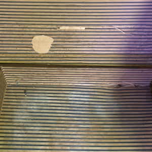 May include: A vintage wooden suitcase with a striped pattern and a small tear in the fabric. The suitcase is closed and has a brown leather handle.