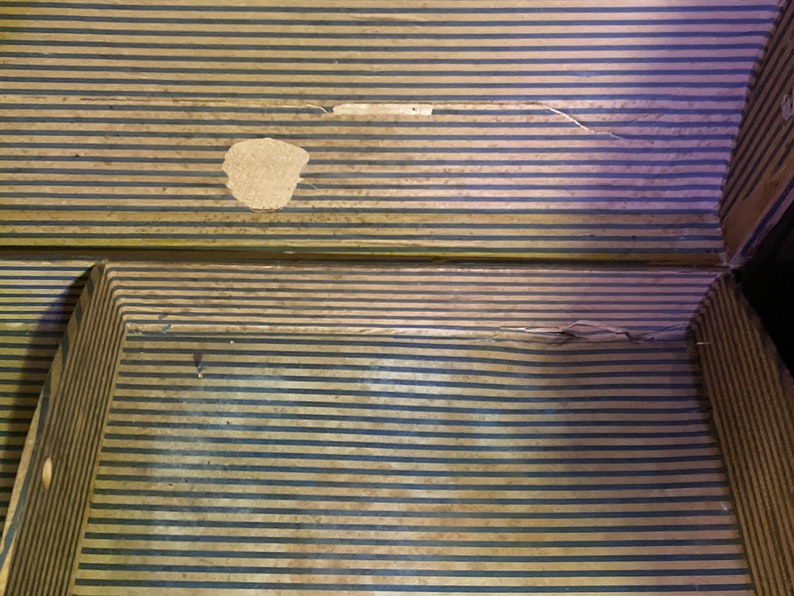 May include: A vintage wooden suitcase with a striped pattern and a small tear in the fabric. The suitcase is closed and has a brown leather handle.