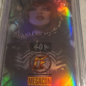 May include: A holographic comic book cover featuring a woman with dark hair and a black and white costume. The cover has a rainbow iridescent effect and the text "Power Hour Preview Edition #2" and "MEGACON".