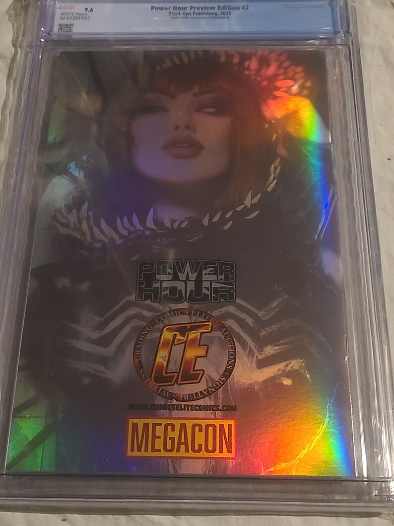 May include: A holographic comic book cover featuring a woman with dark hair and a black and white costume. The cover has a rainbow iridescent effect and the text "Power Hour Preview Edition #2" and "MEGACON".