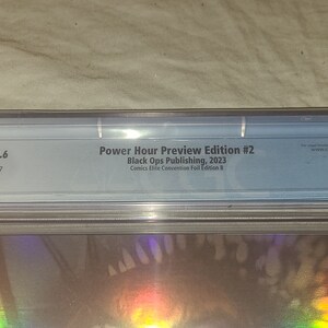 May include: A CGC graded comic book with a 9.6 rating. The comic is titled "Power Hour Preview Edition #2" and is published by Black Ops Publishing in 2023. The comic is a Comics Elite Convention Foil Edition B.