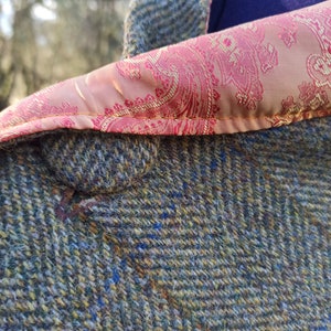 May include: Close-up of a tweed jacket with a paisley patterned lining. The jacket is a mix of green, blue, and yellow threads. The lining is a light pink with a red and gold paisley design. A blue polka dot scarf is visible.