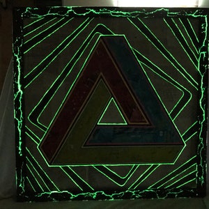 May include: A framed artwork with a green, yellow, red, and blue geometric triangle design. The frame is black and has a green glow around the edges.