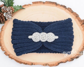May include: Navy blue knitted headband with a silver jeweled embellishment. The headband is on a wooden surface.