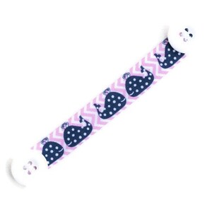May include: A pink and white chevron patterned mask extender with a navy blue whale print. The extender has white buttons on each end.