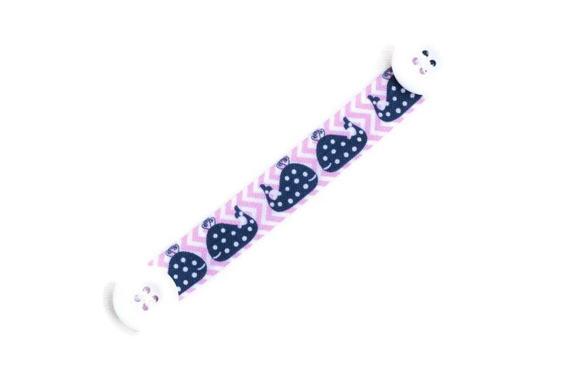 May include: A pink and white chevron patterned mask extender with a navy blue whale print. The extender has white buttons on each end.