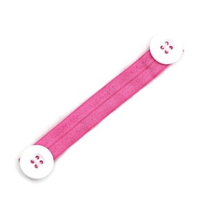 May include: Pink elastic strap with two white buttons for holding a face mask.