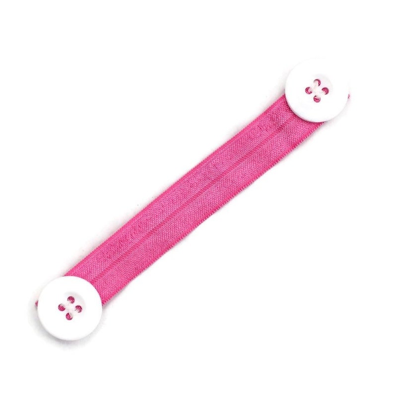 May include: Pink elastic strap with two white buttons for holding a face mask.