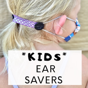 May include: Purple and white patterned fabric ear savers with black buttons. The ear savers are attached to a face mask. The text "*KIDS* EAR SAVERS" is on a white background.