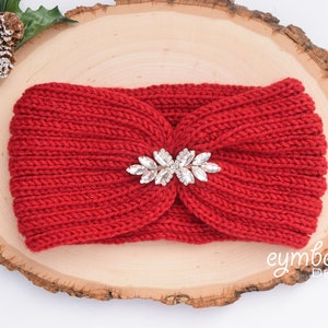 May include: Red knitted headband with a sparkly silver leaf-shaped embellishment. The headband is on a wooden surface.