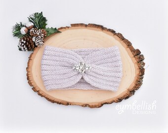 May include: A light purple knitted headband with a large, sparkly, silver-toned rhinestone embellishment in the center.