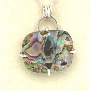May include: A silver pendant with a large, iridescent abalone shell. The shell has a unique pattern of blues, greens, and browns. The pendant is attached to a silver chain.