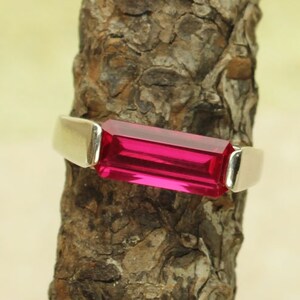 May include: A silver ring with a rectangular, bright pink gemstone.